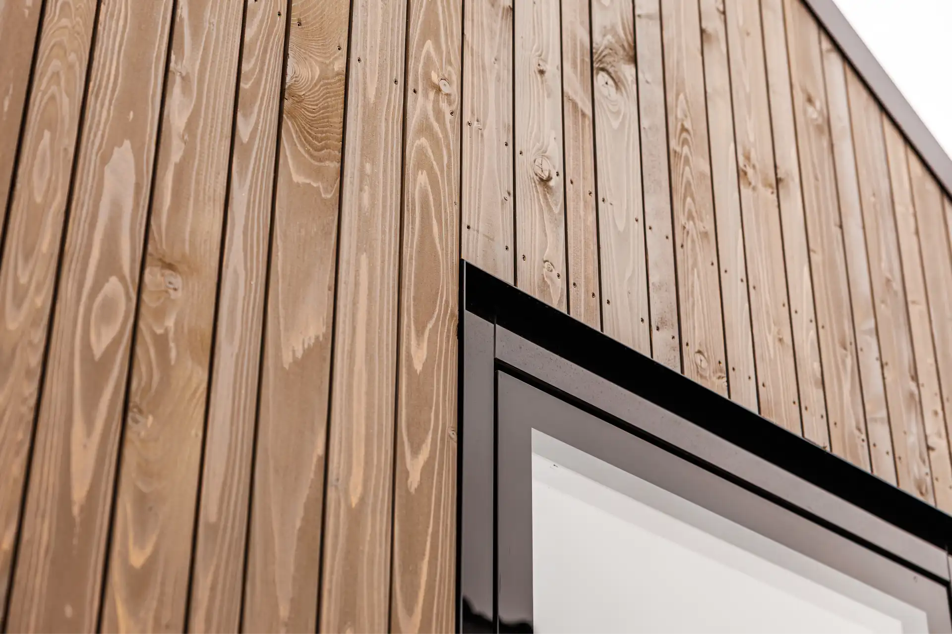Detail einer Hausfassade mit senkrecht angeordneten Holzprofilen und Fenster